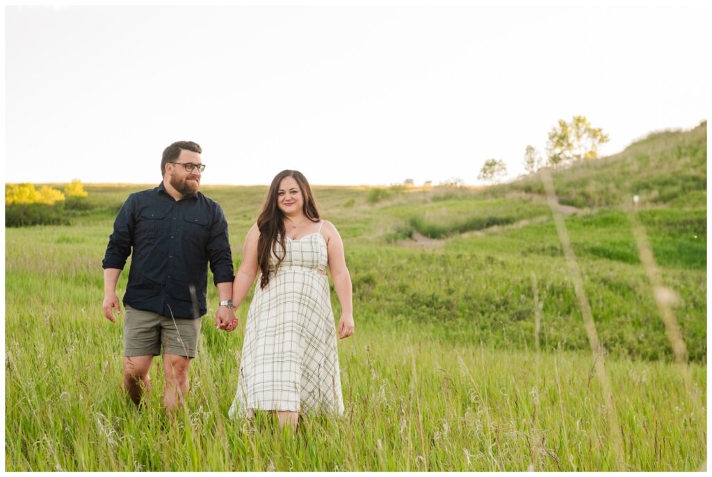 Dustin & Kristyn - Wascana Trails Engagement - 04- Couple walks through tall grass