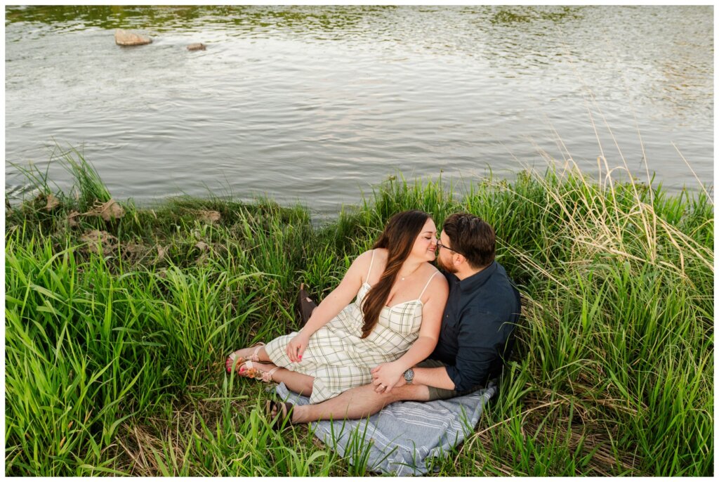 Dustin & Kristyn - Wascana Trails Engagement - 08 - Couple sits on blanket on the riverbank