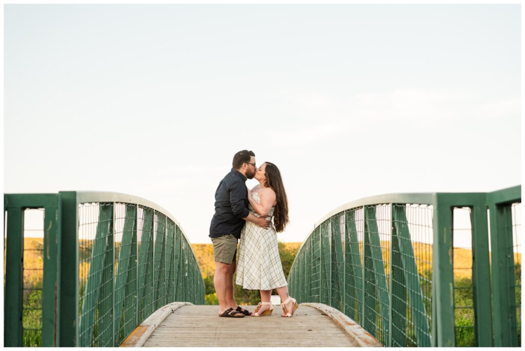 Dustin & Kristyn - Wascana Trails Engagement - 10 - Engaged couple kisses on green bridge