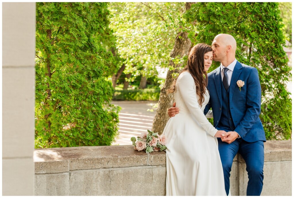 Remi & Celine - Regina Wedding - Holy Rosary Cathedral - 10- Couple sits on the brick wall