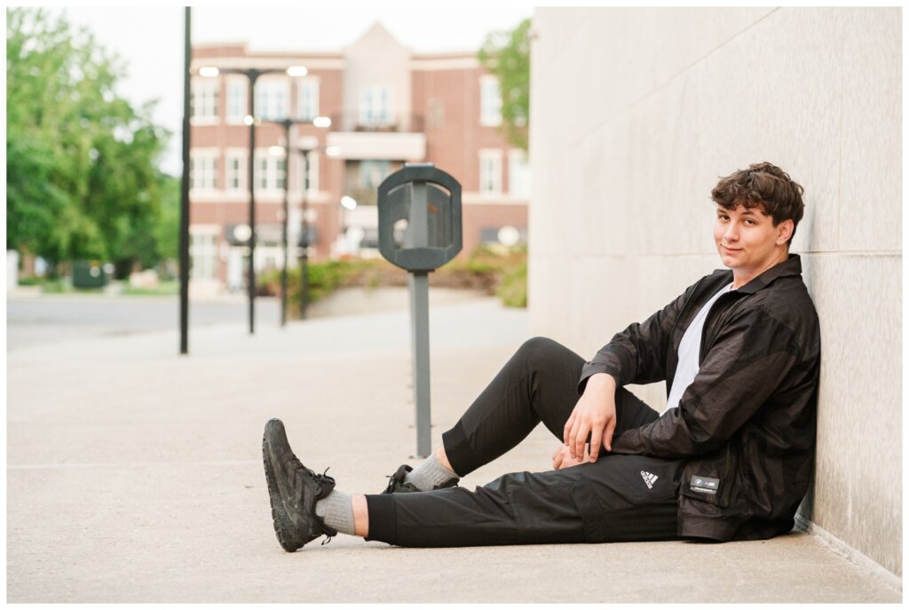 Zach - Senior Grad Session - Provincial Archives of Saskatchewan - 08 - Grad sits up against wall in black bomber jacket