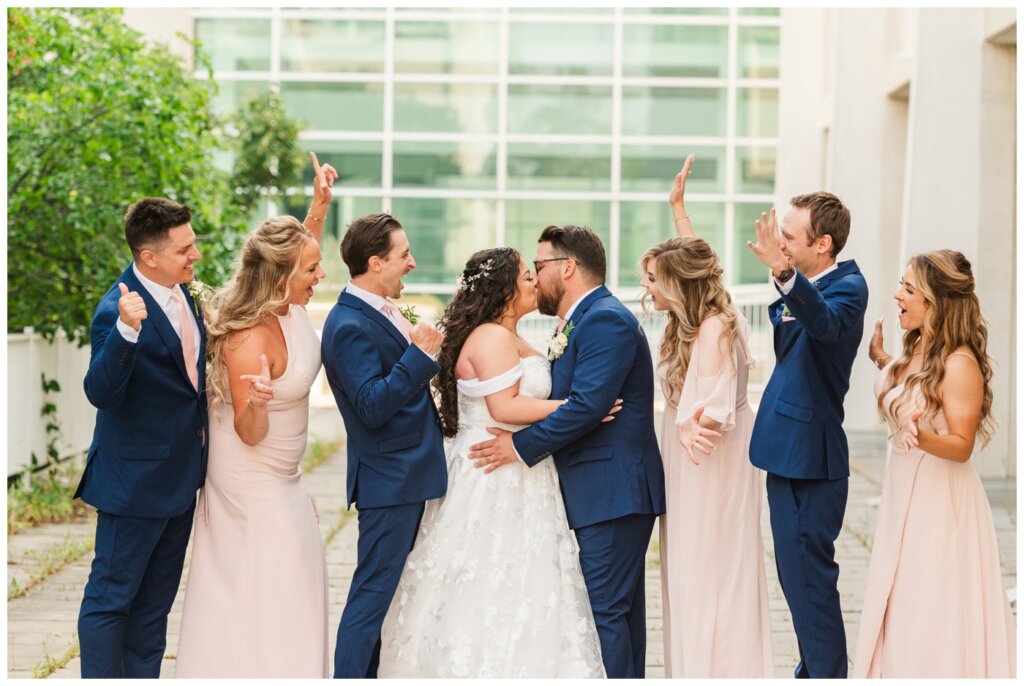 Dustin & Kristyn - Regina Wedding - 18 - University of Regina - Wedding party cheers as couple kiss