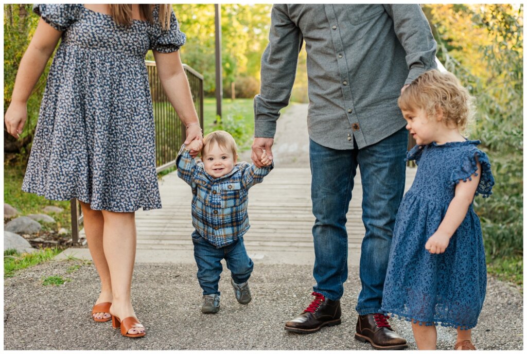 Filby Family 2024 - Regina Family Photography - 03 - Wascana View Park - Toddler boy holds hands with his parents