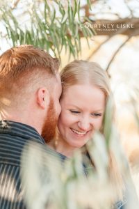 Engaged woman laughs with her fiancee under willow tree