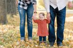 Little girl holding hands with her mom and dad in yellow leaves