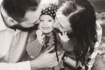 Mom and dad squishing little girls face with kisses