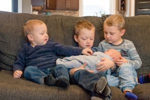 Three older brothers sit with new little brother on the couch