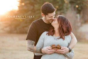 Couple kiss at sunset while holding brown baby shoes