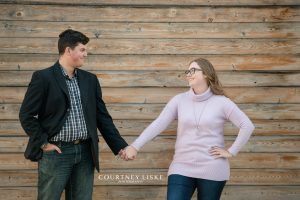 Couple stand holding hands against shiplap barnwood wall