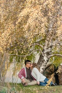 Man in white and red striped sweater kisses fiance under willow tree