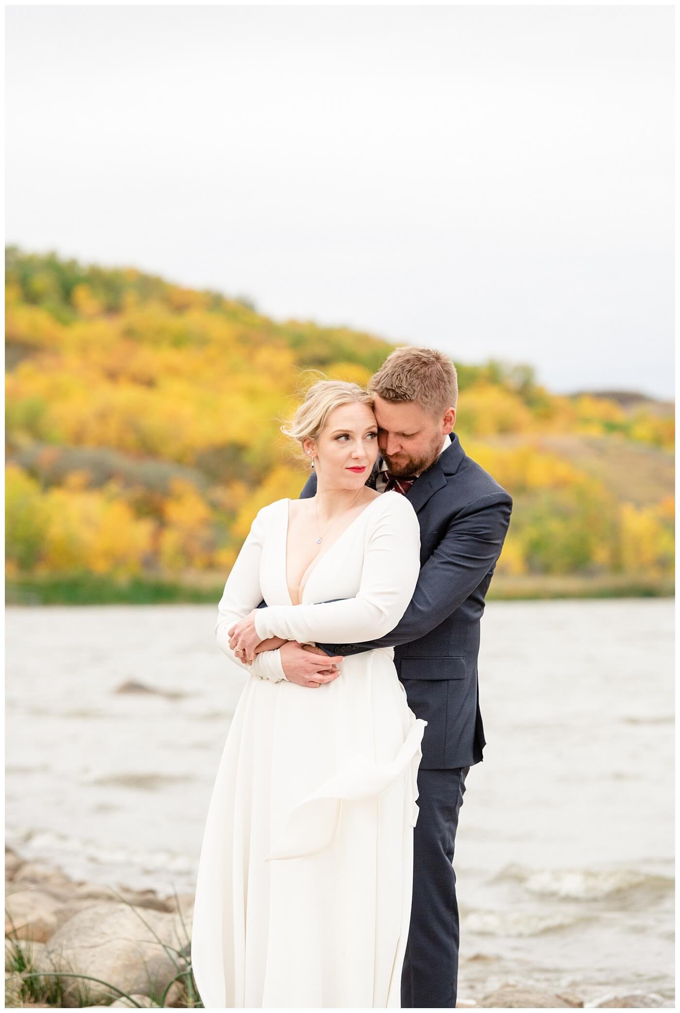 Regina Wedding Photographer - Tyrel - Allison - Bride looks out over the water as her Groom embraces her