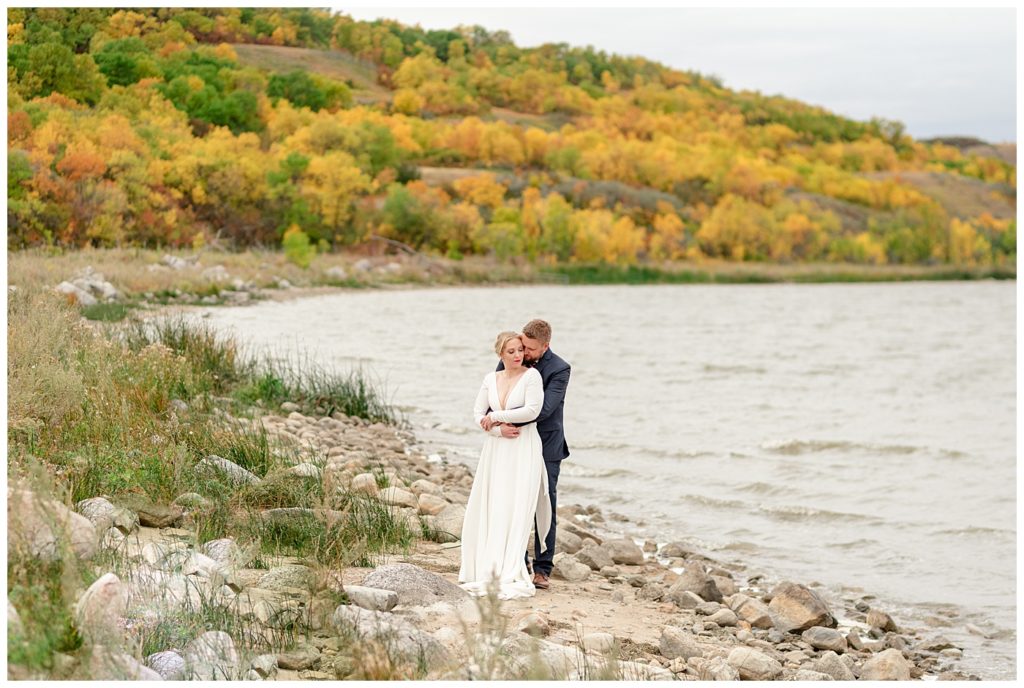 Regina Wedding Photography - Tyrel - Allison - Bride & Groom beside the water among the fall colours of the valley