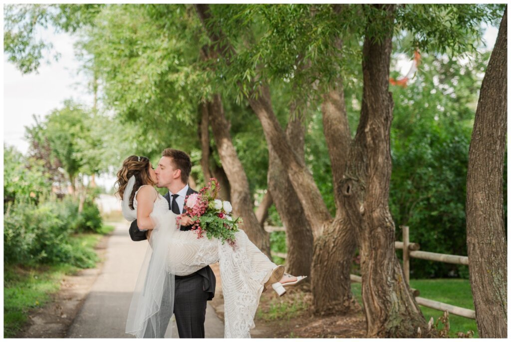 Taylor & Jolene - Emerald Park Wedding - 16 - Groom carries bride down tree lined path