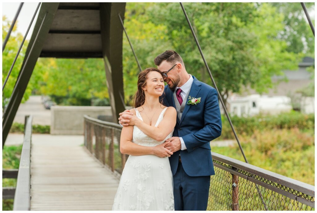 Andrew & Lacey - 24 - Groom nuzzling into bride's ear at bridge at Rotary Park