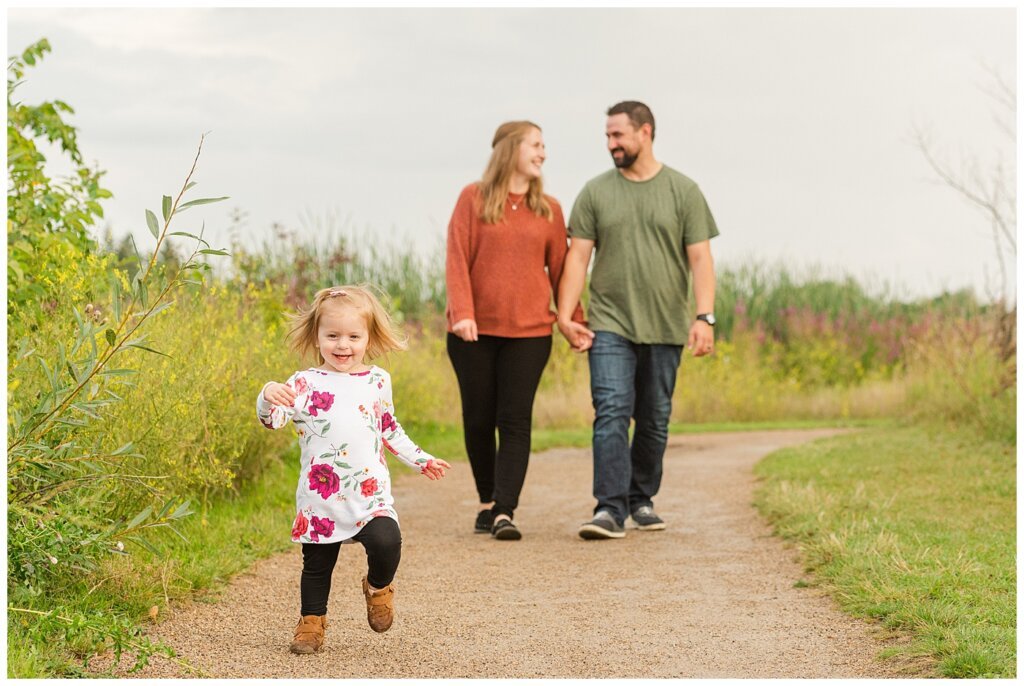 Eyre Family 2021 - AE Wilson Park - Family Photo Shoot - 14 - Mom and dad share a moment as daughter runs ahead