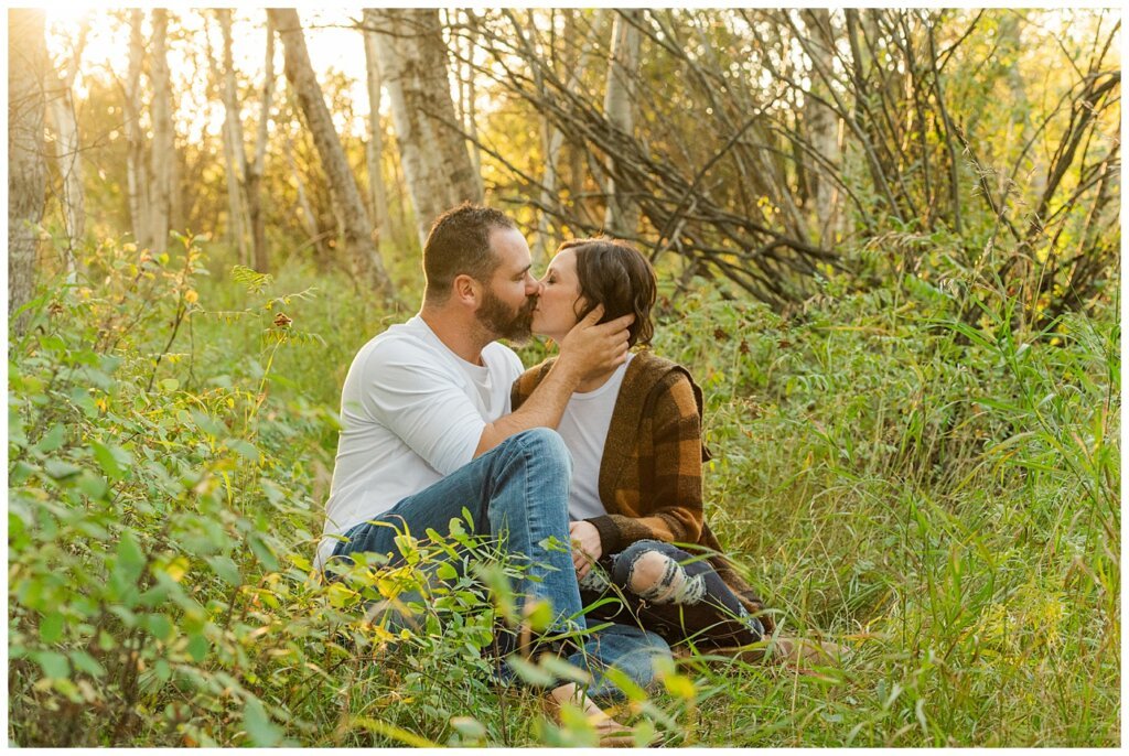 Kim & Lisa Korchinski - White Butte Trails - Family Photo Session 2021 - 07 - Husband and wife kiss, sitting on ground at white butte trails