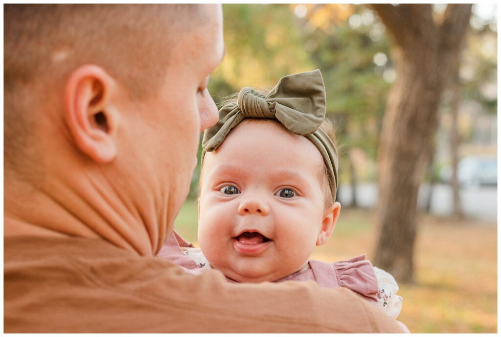 Filby Family - Regina Family Photography - Wascana Park - 05 - Isla smiling at camera over dad's shoulder