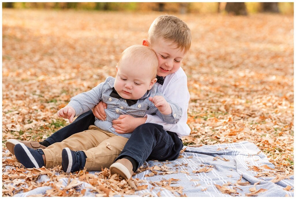 Nickel Family - Regina Science Centre - Family Photo Session - 04 - Older brother huggin infant on blanket