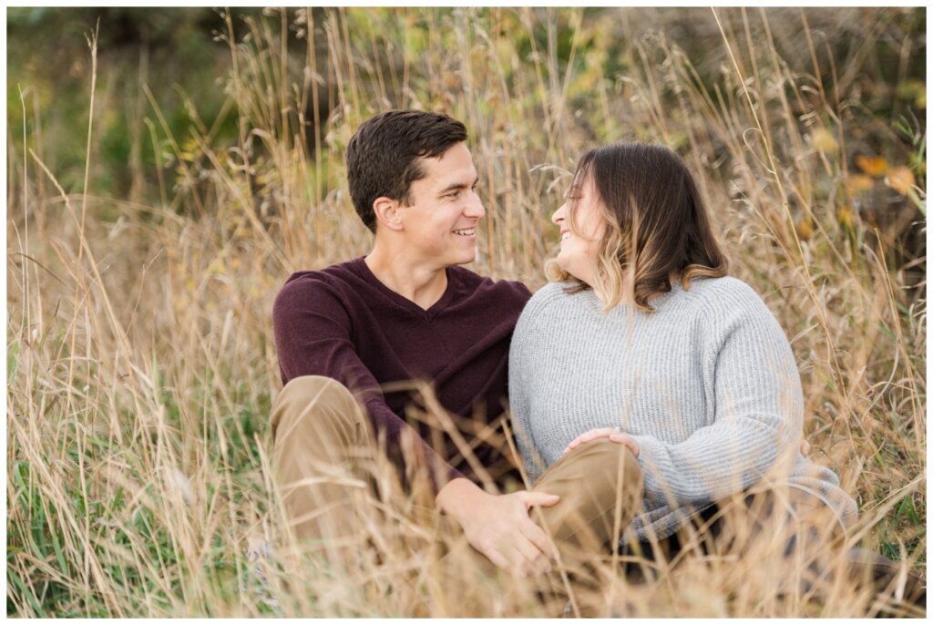 Regina Engagement Photography - Ben & Megan - Engagement Session at AE Wilson Park and Island - 02 - Couple laughing together while sitting