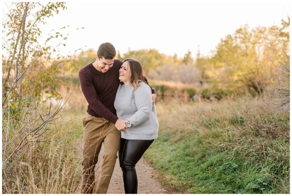 Regina Engagement Photography - Ben & Megan - Engagement Session at AE Wilson Park and Island - 06 - Couple stumbling and laughing as they walk through the park