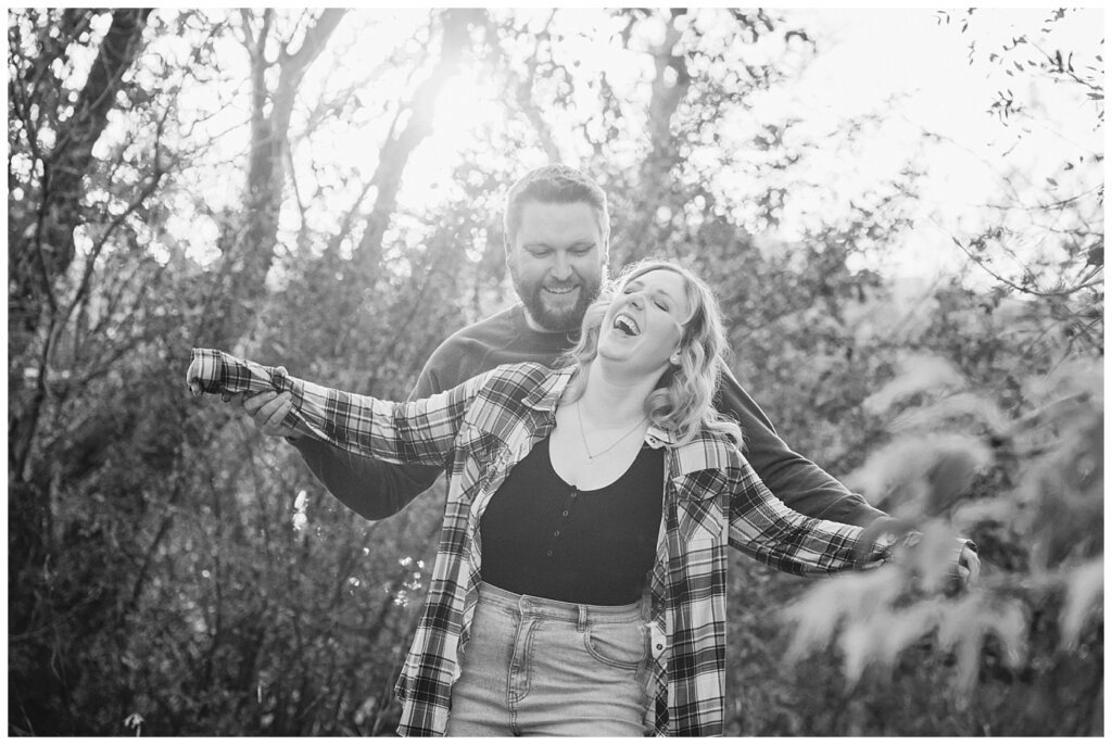 Tyrel & Allison - Regina Anniversary Session - Douglas Park Hill - 06 - Husband making wife laugh as he uses her arms like an airplane