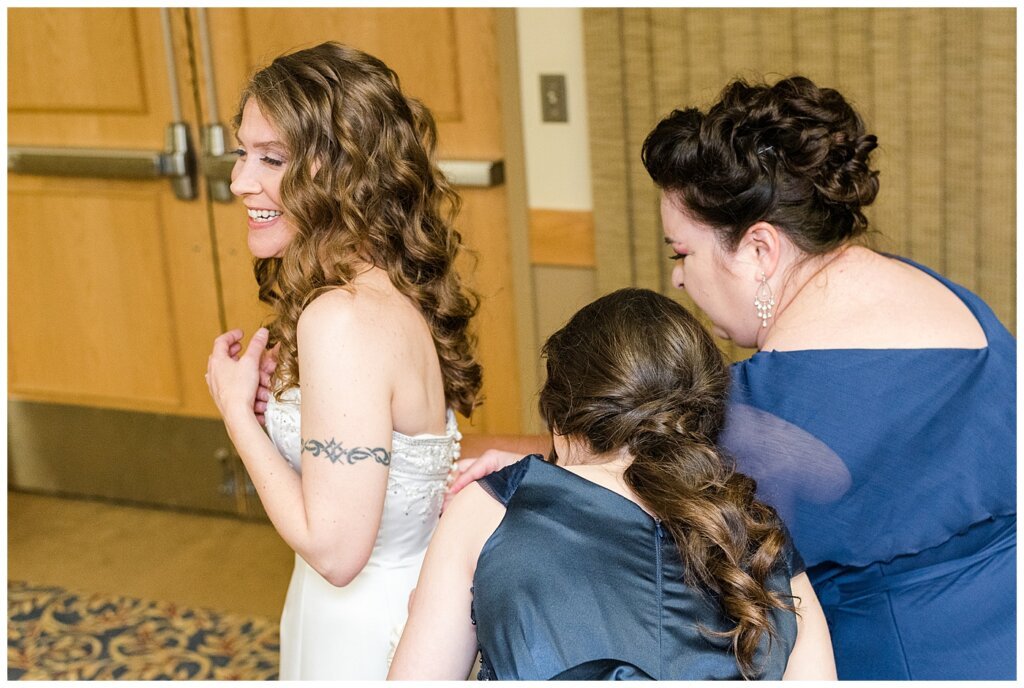 Matt & Ruth - 2022 Wedding - Queensbury Convention Centre - Regina Wedding - Bridesmaids help with dress buttons