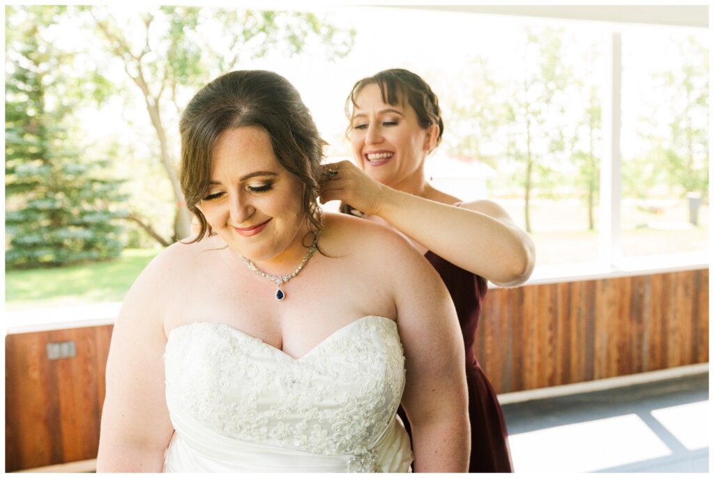 Ben & Megan - 06 - Regina Wedding - Sister helps bride with necklace