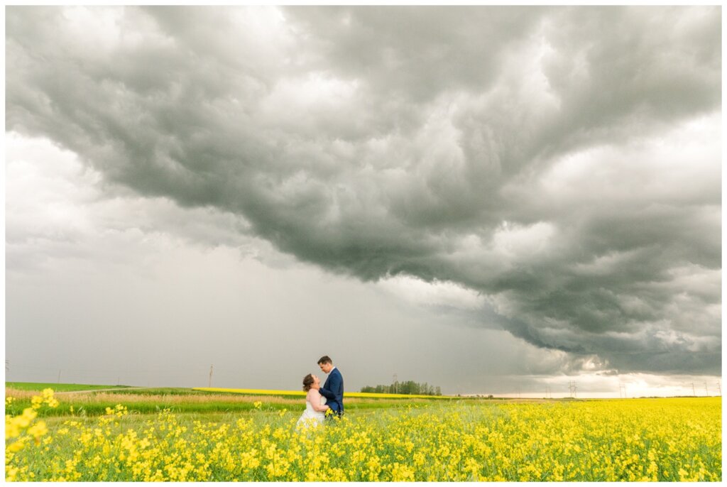 Ben & Megan - 29 - Regina Wedding - Bride & Groom in canola field by storm clouds