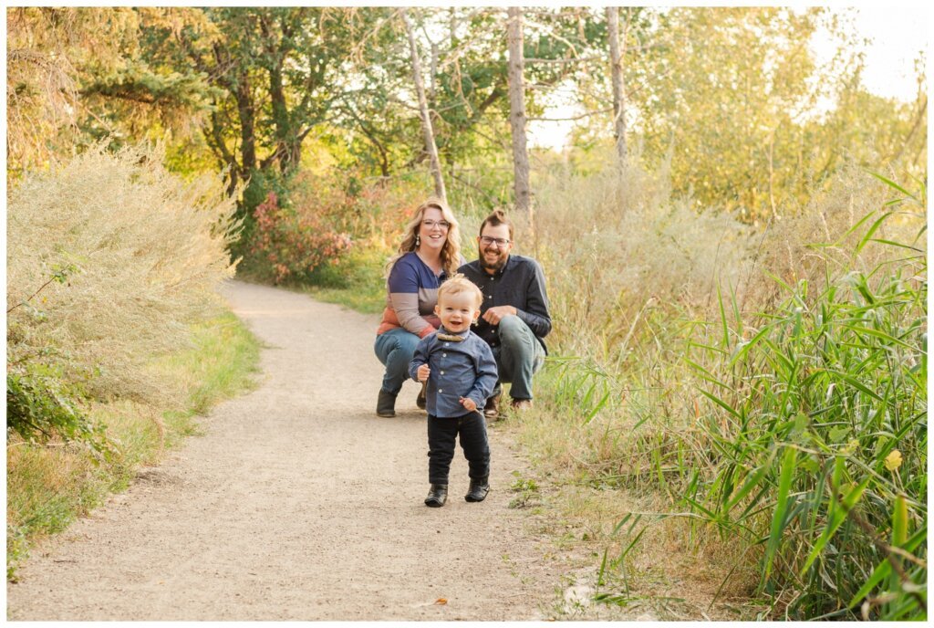 Moffatt Family - 02 - Regina Family Session - Parents watch as their little boy with a bow tie walks down trail