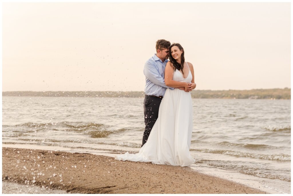 Tris & Jana - 04 - Regina Encore Session - Groom embraces his bride on the beach