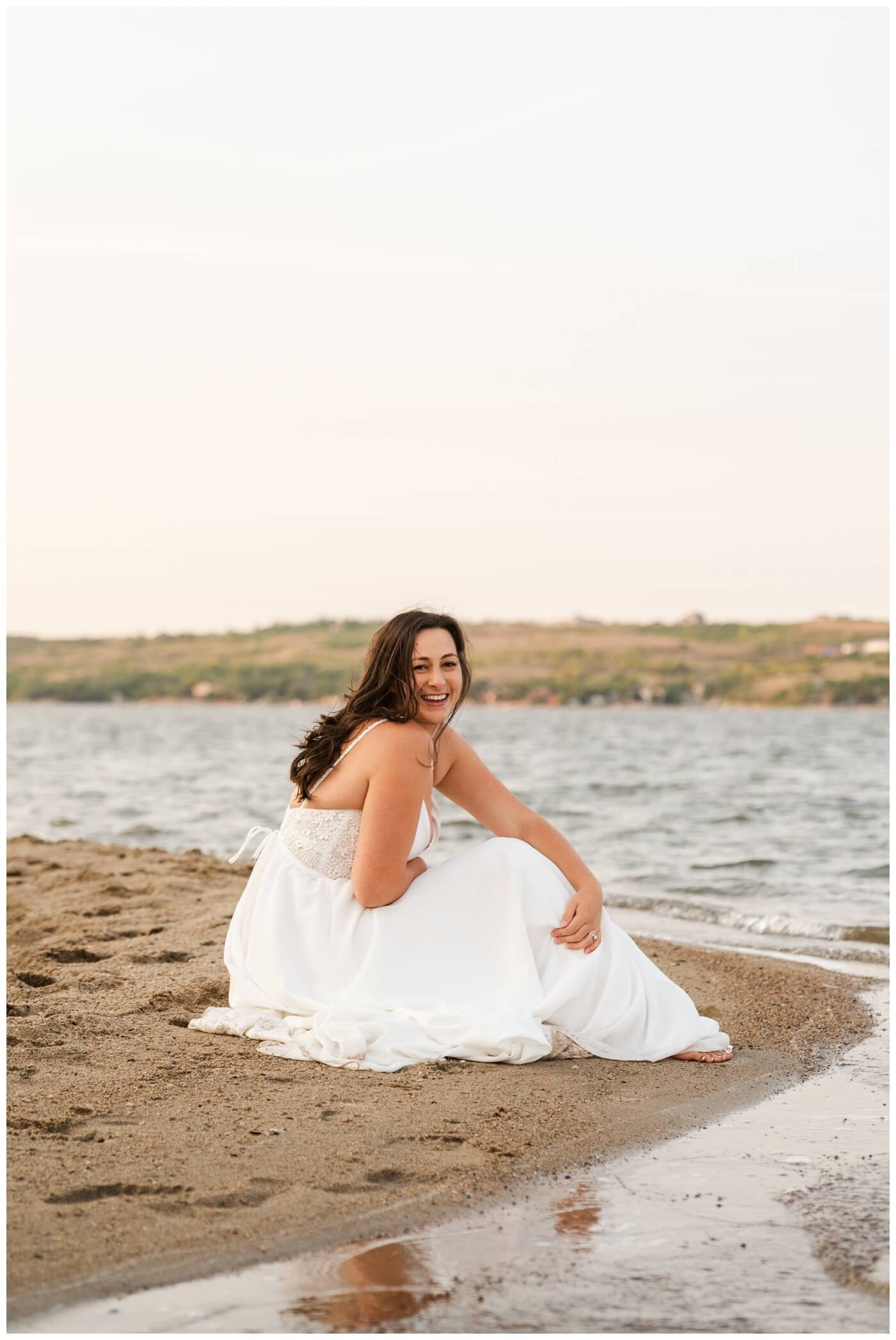 Tris & Jana - 08 - Regina Encore Session - Bride sits in the sand near the water