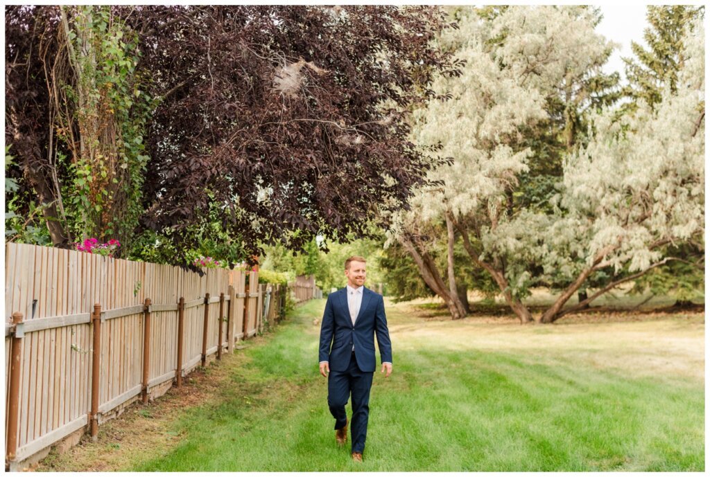 Adam & Caitlin - 03 - Regina Wedding - Groom in his navy blue suit walking through the park