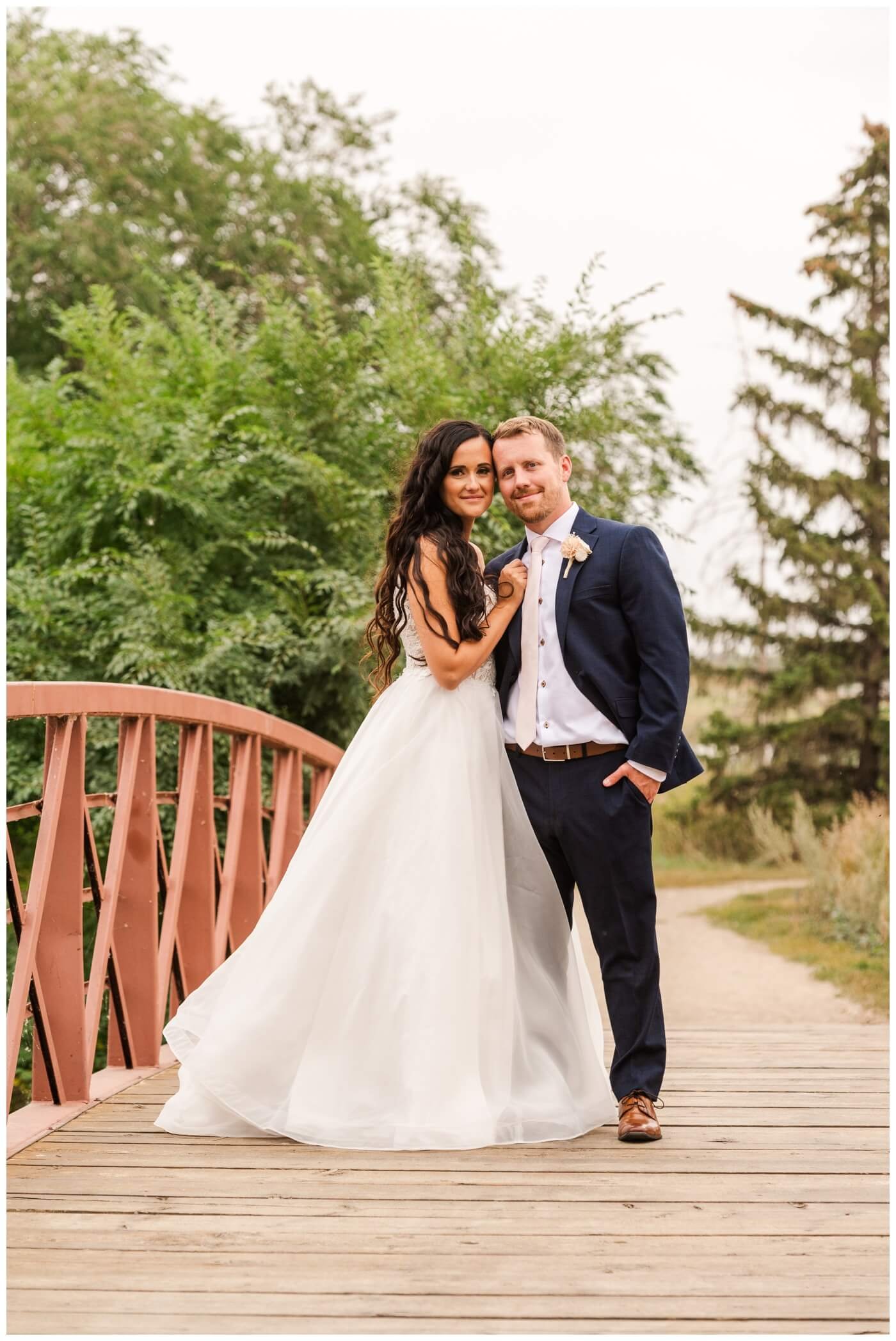 Adam & Caitlin - 29 - Regina Wedding - Bride & Groom stand on bridge in AE Wilson Park