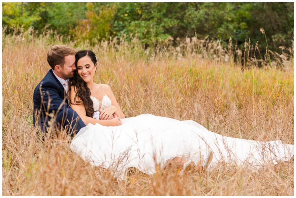 Adam & Caitlin - 31 - Regina Wedding - Bride & Groom sit in the tall grass