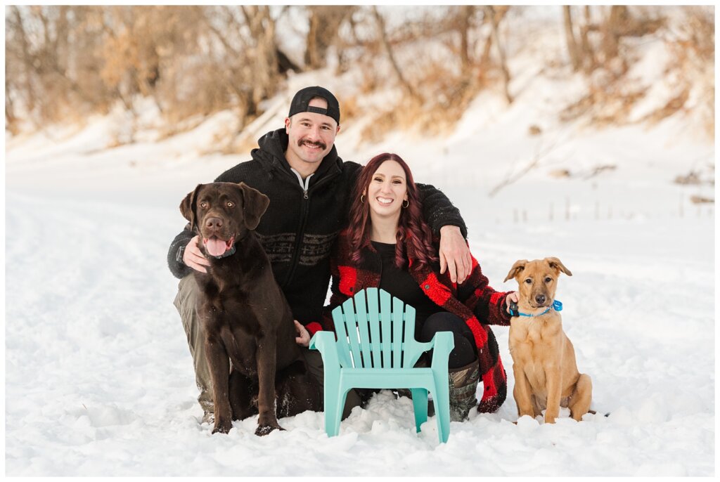 Brett & Brittany - Winter 2023 - Lumsden Valley - 06 - Couple sits with dogs and baby Adirondack chair