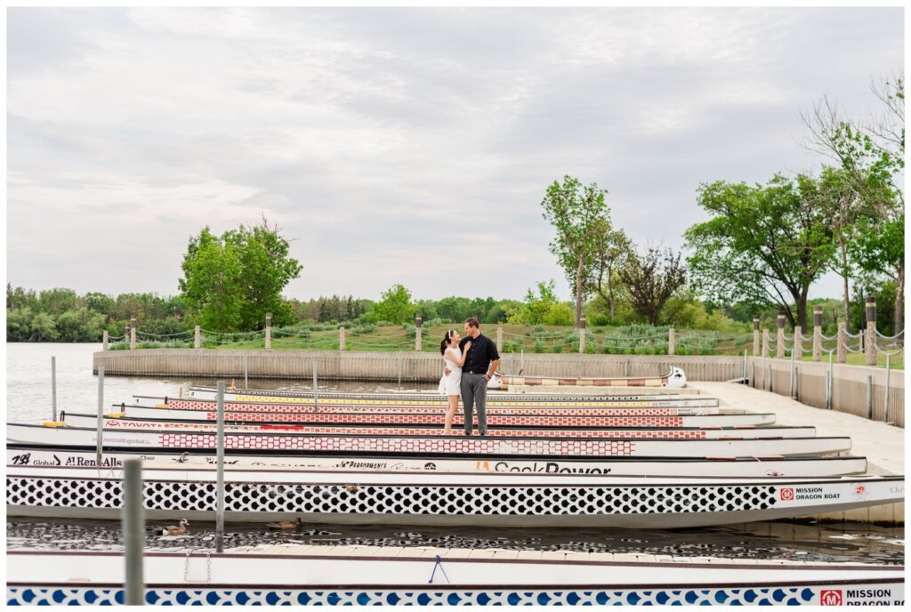 Skylar & Michaela- Regina Engagement - Wascana Park - 001 - Couple stand on dock by dragon boats